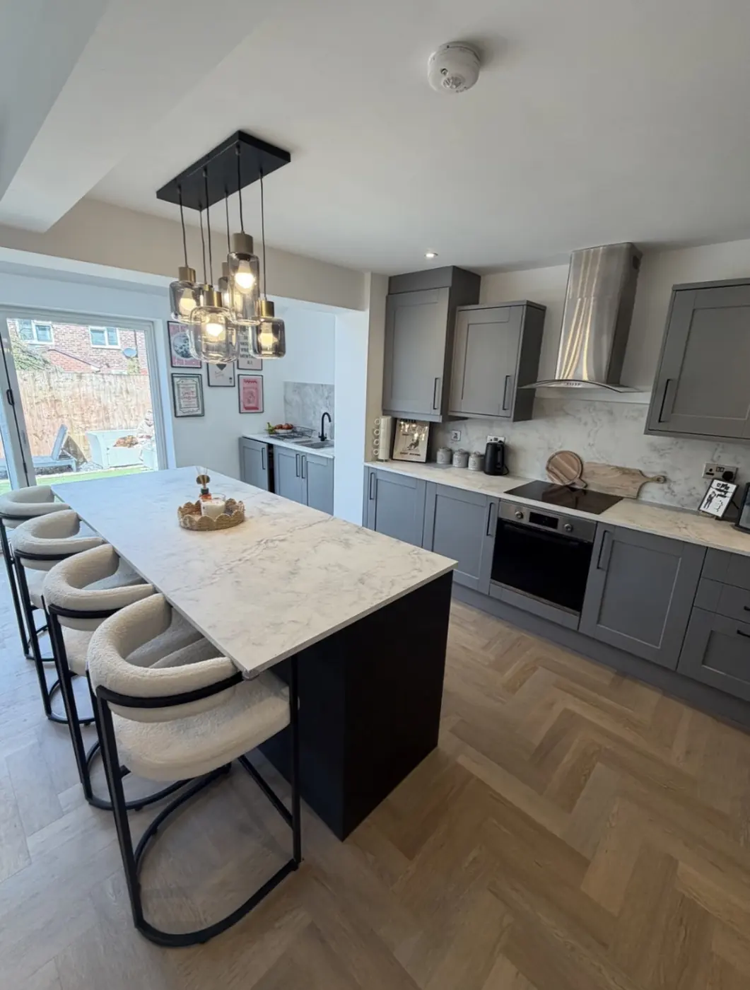 Grey shaker kitchen with dark island, pendant lights and bar stools